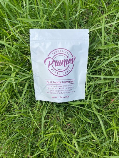 A stand-up pouch of Prunies prune Based Fruit Snack Gummies placed on green grass.